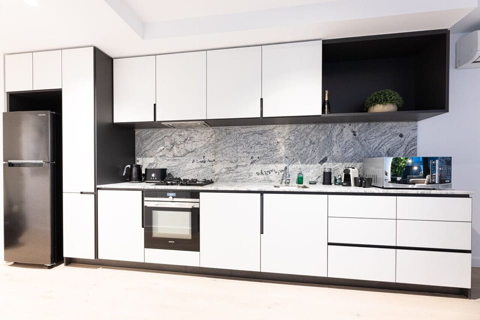 Fully equipped kitchen with white handleless cabinetry, a dramatic marble splashback, gas cooktop, oven, Samsung fridge, Nespresso machine, and microwave — everything needed for a comfortable self-catered stay.