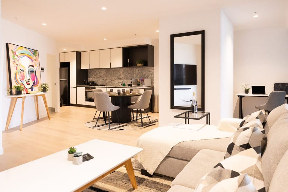 Open-plan living space with a bold pop-art canvas, fully equipped kitchen, round dining table, and a dedicated workspace. Light timber floors and a large floor mirror keep the layout feeling spacious and well-lit.  *(212 characters)*