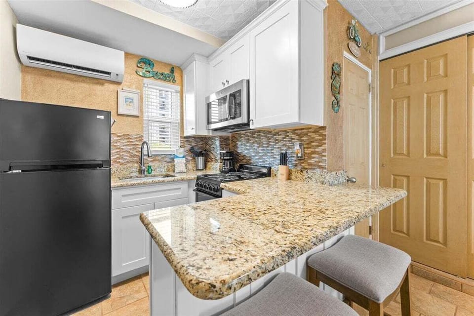 Fully equipped kitchen with granite counters, mosaic tile backsplash, stove, microwave, fridge, coffee maker, and breakfast bar seating — everything you need for a home-cooked meal.