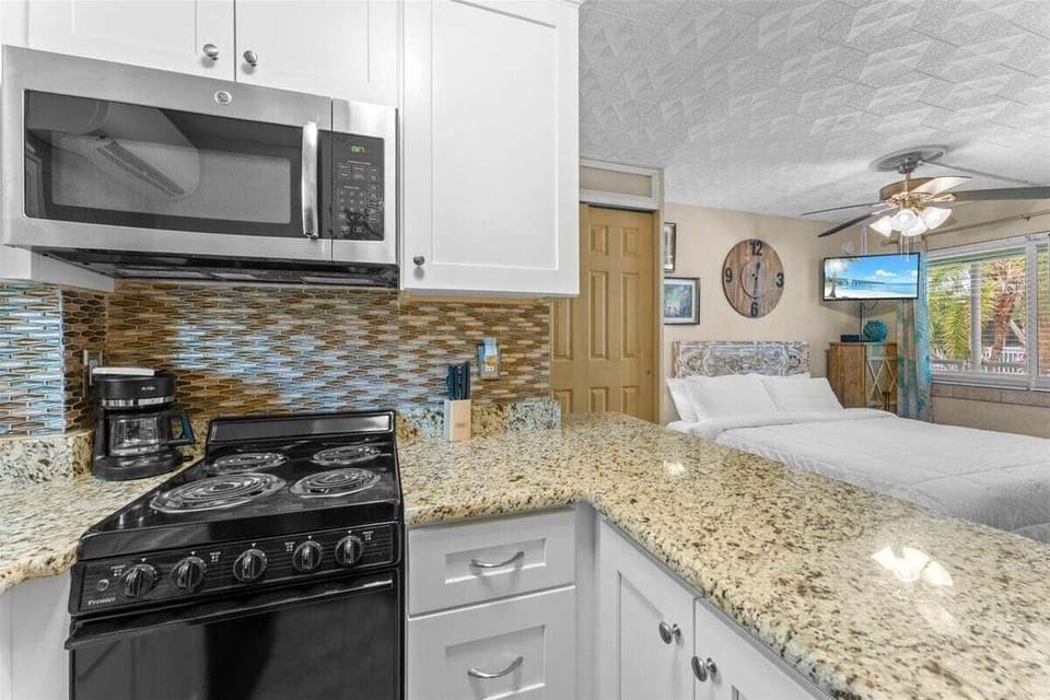 Fully equipped kitchen with granite counters, mosaic tile backsplash, stove, microwave, fridge, coffee maker, and breakfast bar seating — everything you need for a home-cooked meal.