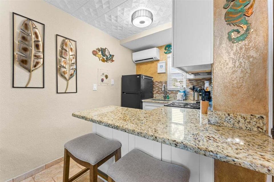 Fully equipped kitchen with granite counters, mosaic tile backsplash, stove, microwave, fridge, coffee maker, and breakfast bar seating — everything you need for a home-cooked meal.