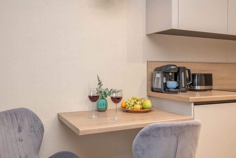 A minimalist dining setup with a vase, fruit bowl, and coffee maker.

