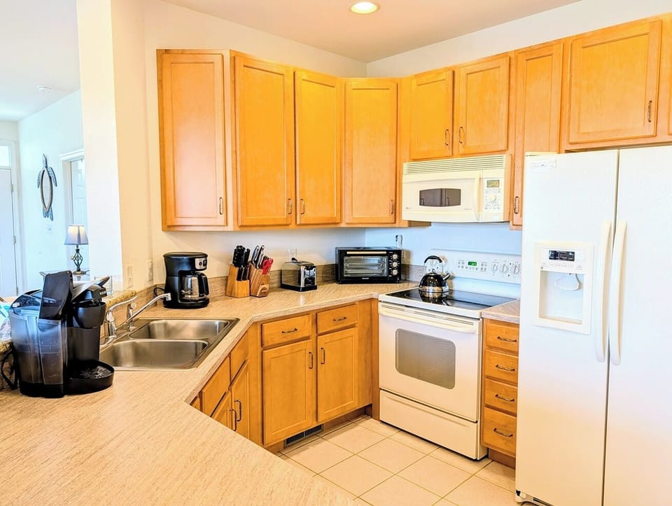128C October Glory Kitchen Interior - Internal perspective of the kitchen at 128C October Glory showcasing ample honey-oak upper and lower cabinets, clean white appliances including a refrigerator and built-in microwave, and tile flooring.