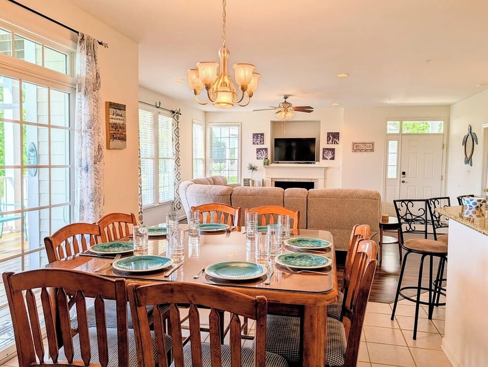 128C October Glory Dining Area to Living Room - Alternate perspective of the dining table at 128C October Glory, highlighting the bright, open floor plan that flows directly into the cozy family living area and breakfast bar seating.