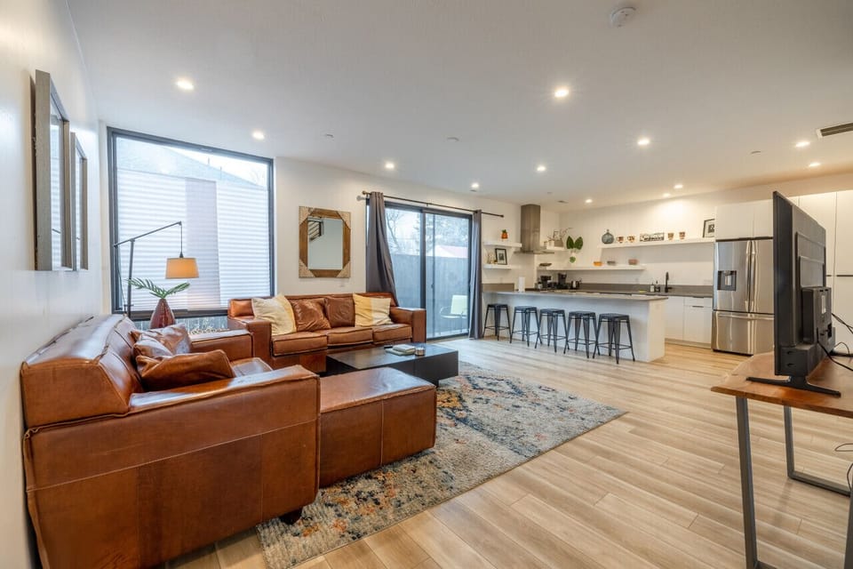Open-concept living and dining area designed for comfort, featuring leather sofas, a large TV, and bright natural light — the ideal gathering space after exploring Salt Lake City or skiing nearby resorts.