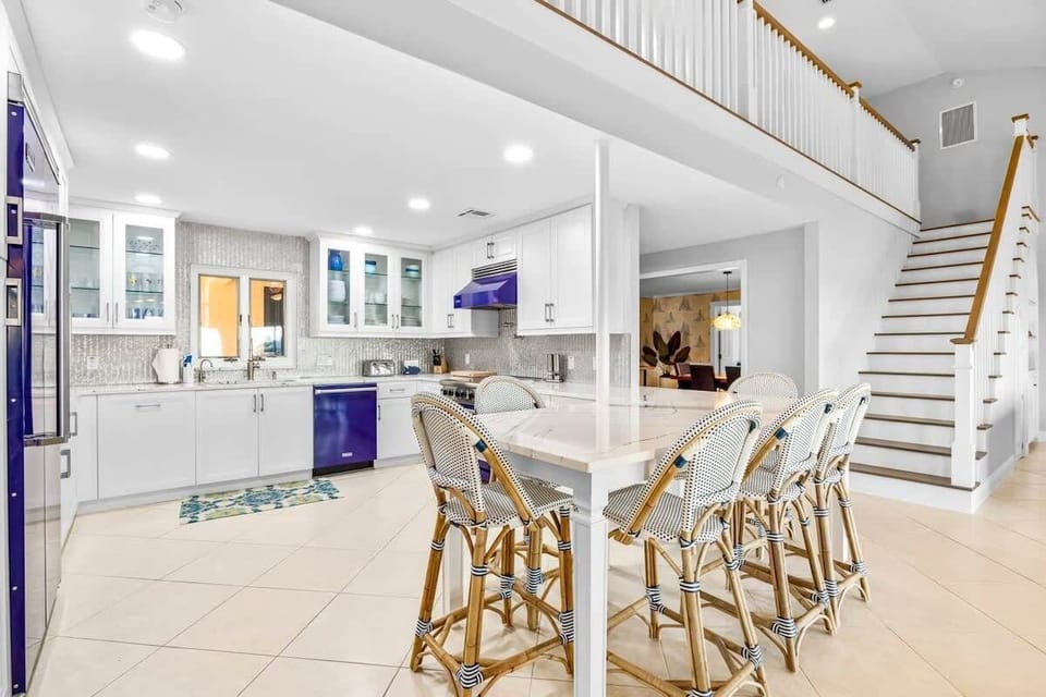 Modern kitchen with a large marble island and blue appliances under a high ceiling.
