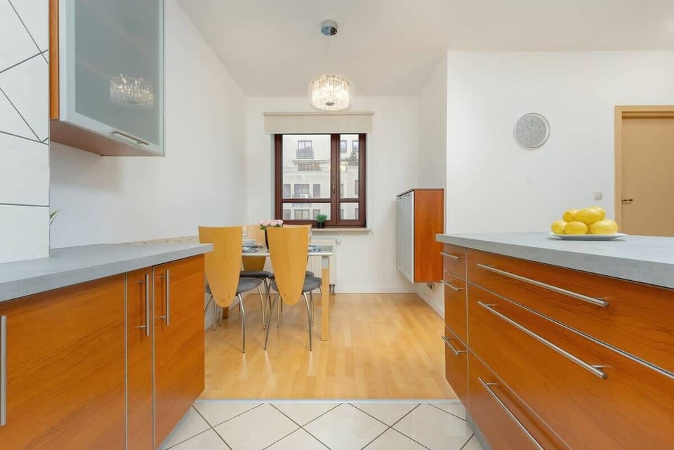 A kitchen with warm wooden cabinetry, white tiled walls, and built-in appliances.