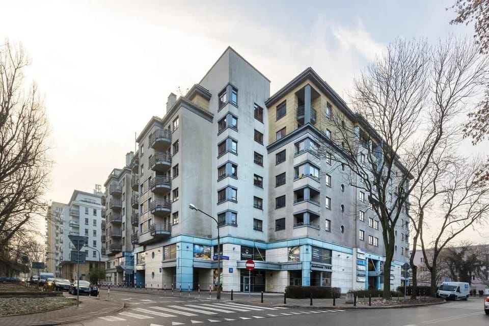 A street view of a modern apartment building with trees and parked cars.