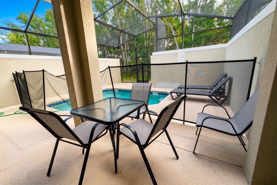 Covered outdoor seating area beside the private screened pool, featuring a table, chairs, and loungers, perfect for relaxing, enjoying a meal, or spending time outdoors with family