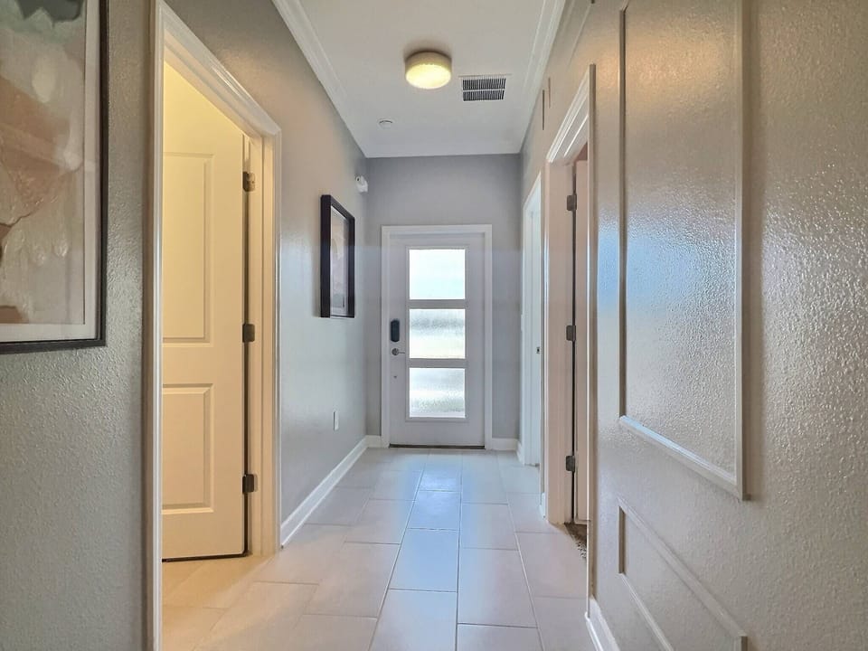 Step into a bright corridor featuring sleek tile flooring that leads to a welcoming entrance, where natural light spills in through the glass door. Framed artwork adds a touch of personality, enhancing the space's modern charm.
