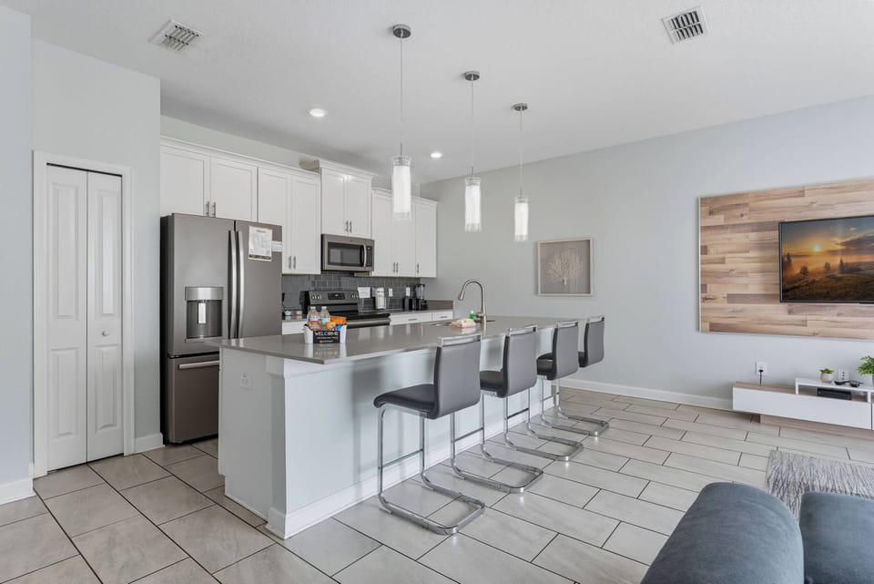Welcome to a stunning kitchen featuring sleek stainless steel appliances and a spacious stone island. Enjoy casual dining on modern bar stools under soft pendant lights, perfect for cooking and socializing in a warm atmosphere.