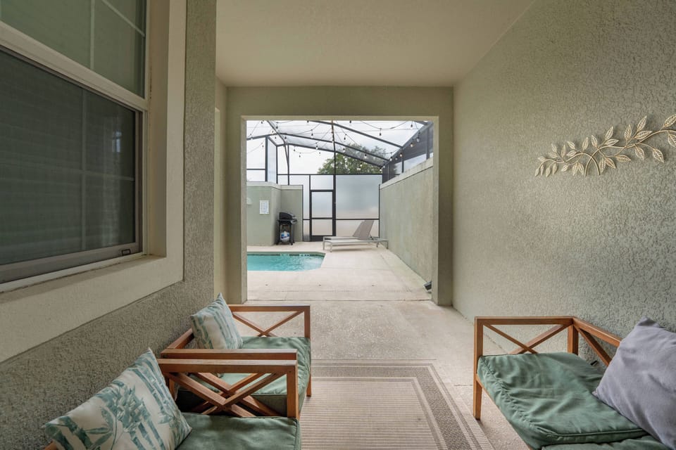 Enter a serene space where natural light brightens soft green walls. Relax in comfortable seating as you enjoy the view of the sparkling pool through the screened enclosure, perfect for unwinding in a peaceful atmosphere.