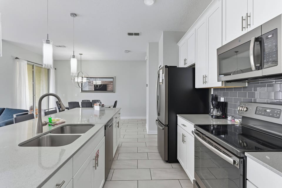 This bright kitchen boasts sleek white cabinetry and a spacious island perfect for casual dining or meal prep. Stainless steel appliances add sophistication, while polished tile flooring ensures easy cleanup for your convenience.