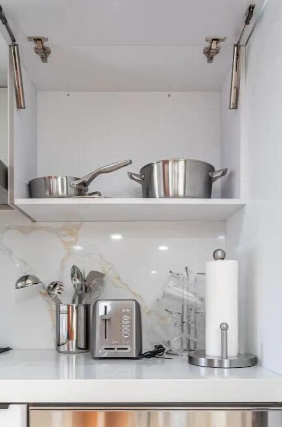 There is a full set of stainless steel cookware in the top cupboard 