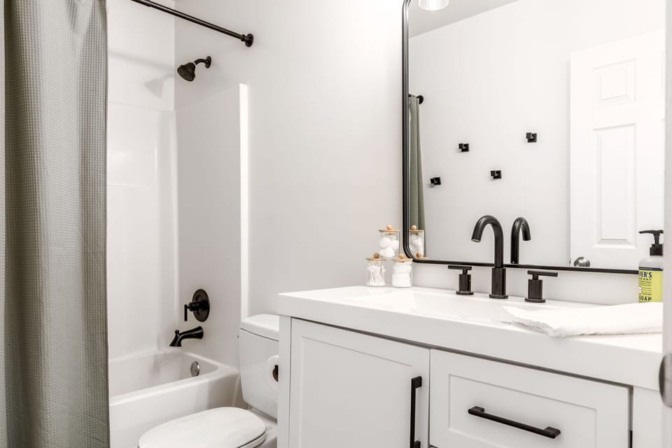 Full bathroom with a bathtub-shower combination, toilet, vanity, and large mirror.