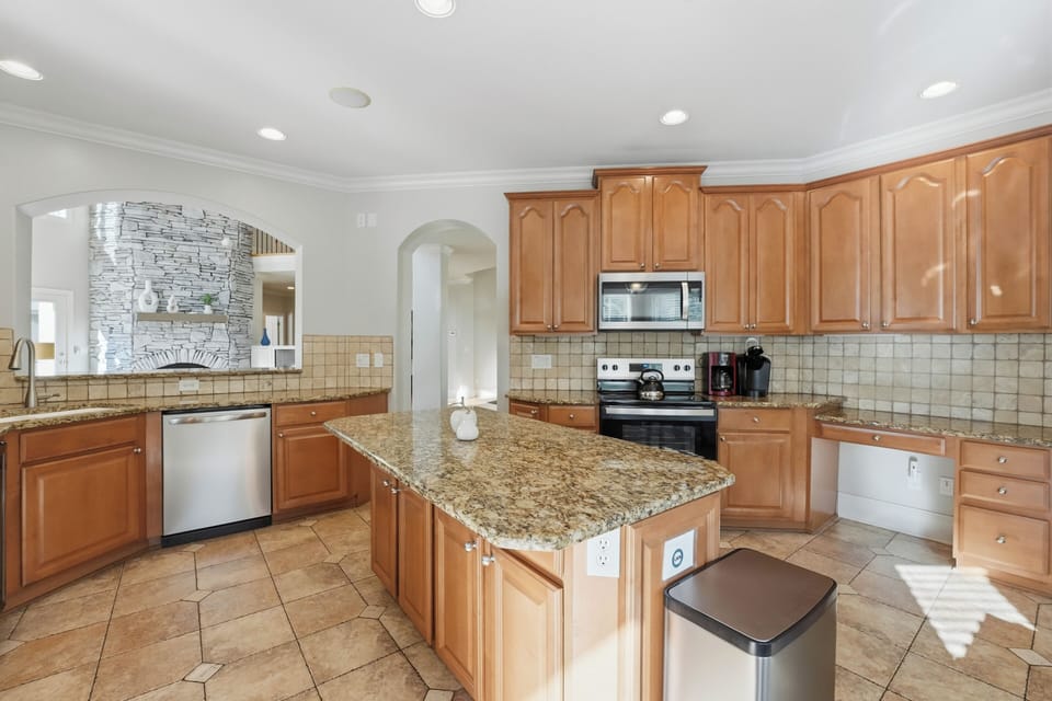 Bright, fully equipped kitchen with granite island seating, stainless steel appliances, and peaceful wooded views.