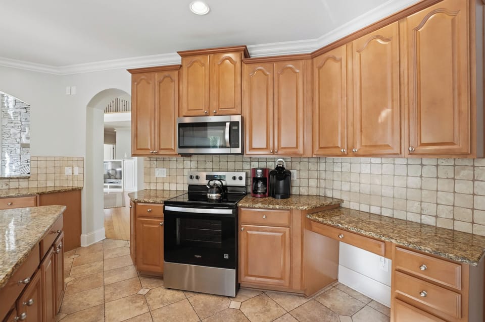 Bright, fully equipped kitchen with granite island seating, stainless steel appliances, and peaceful wooded views.