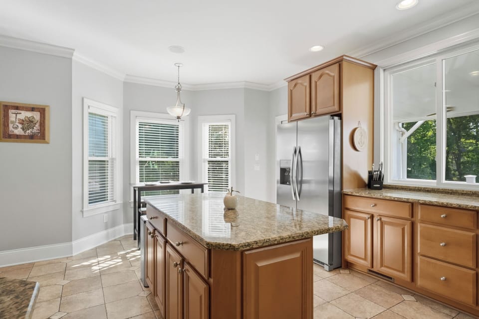 Bright, fully equipped kitchen with granite island seating, stainless steel appliances, and peaceful wooded views.