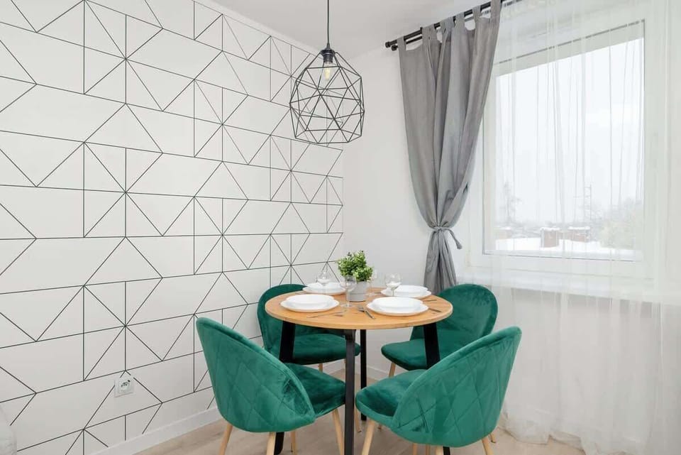 A compact dining area with a small round table, two green chairs, and a white geometric-patterned wall.