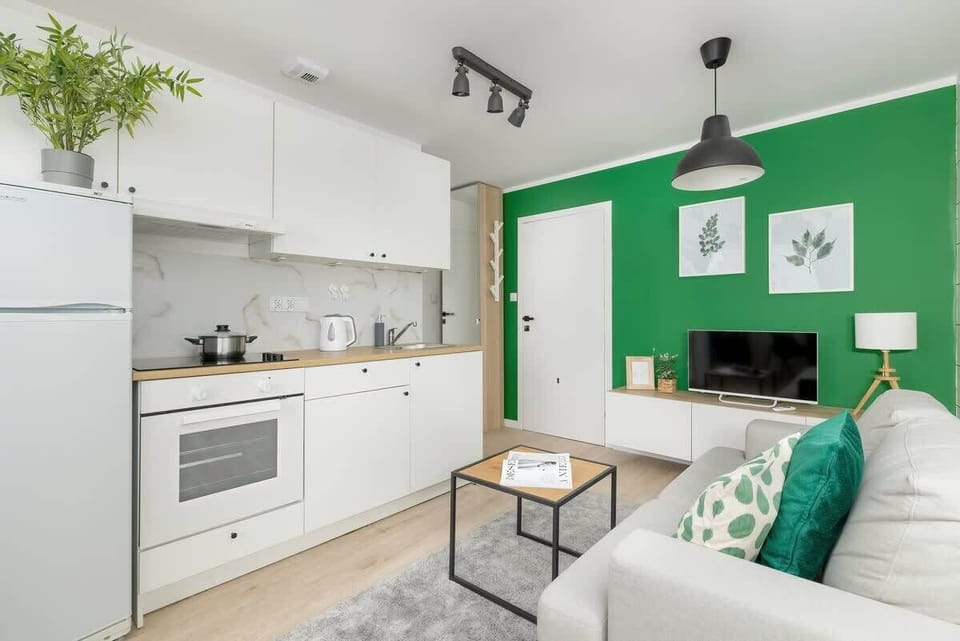 A modern kitchen with white cabinets, a green accent wall, and small potted plants.