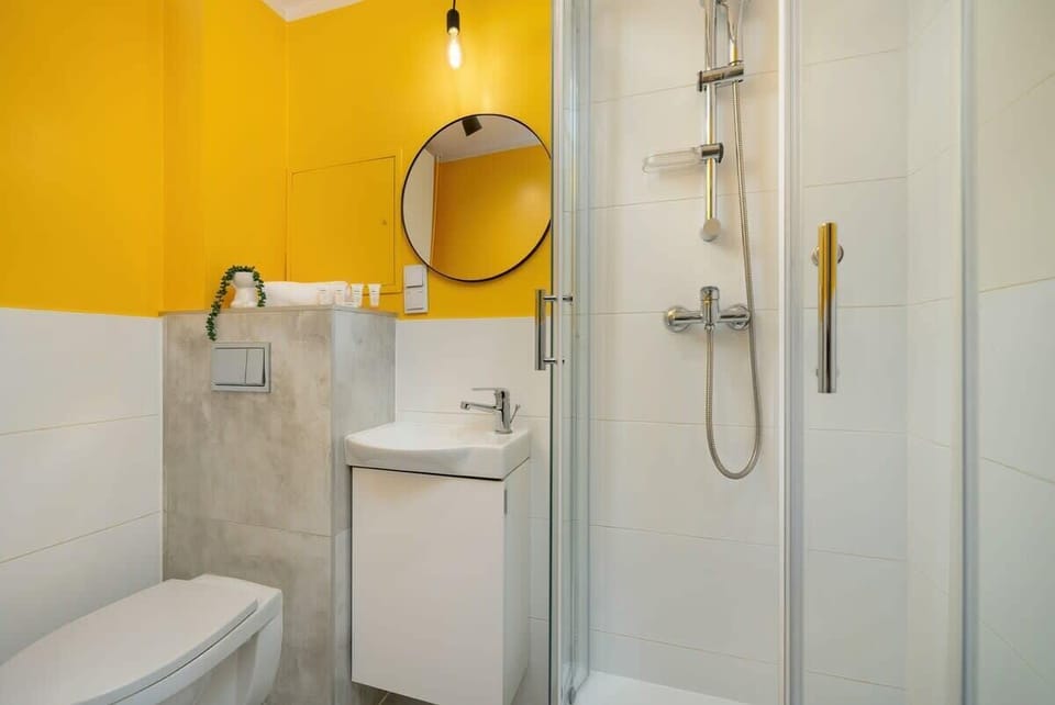 A modern bathroom with yellow accents, a round mirror, and white fixtures.