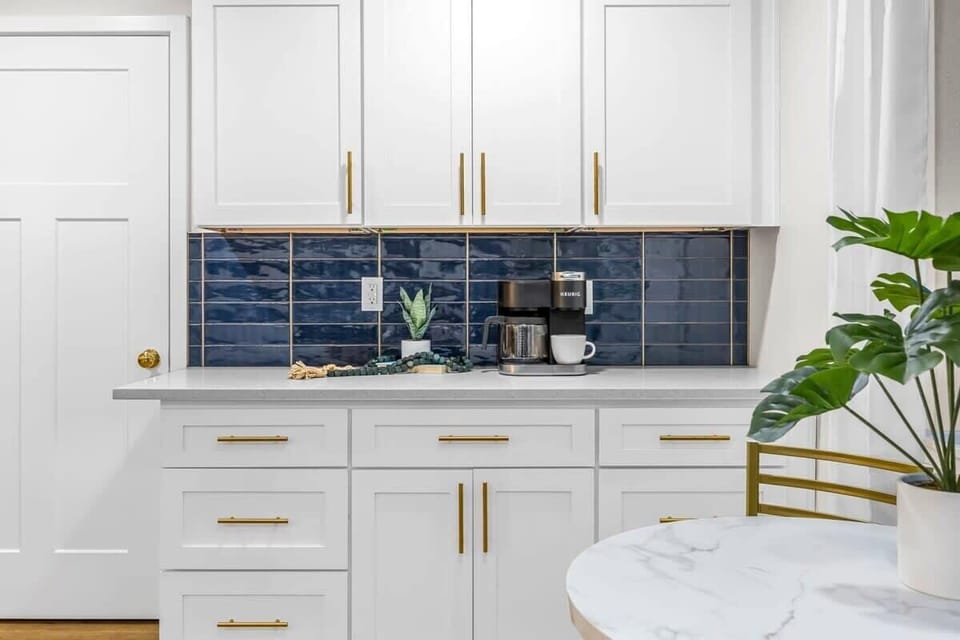 Modern kitchen counter with white cabinetry, gold hardware, and a navy tile backsplash.