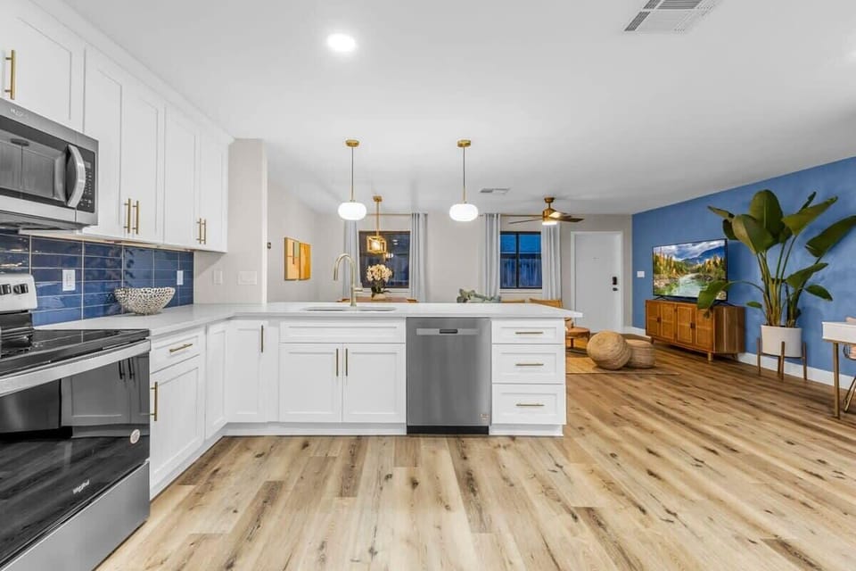 Modern kitchen with white cabinetry and blue tile backsplash opening to a cozy living area.