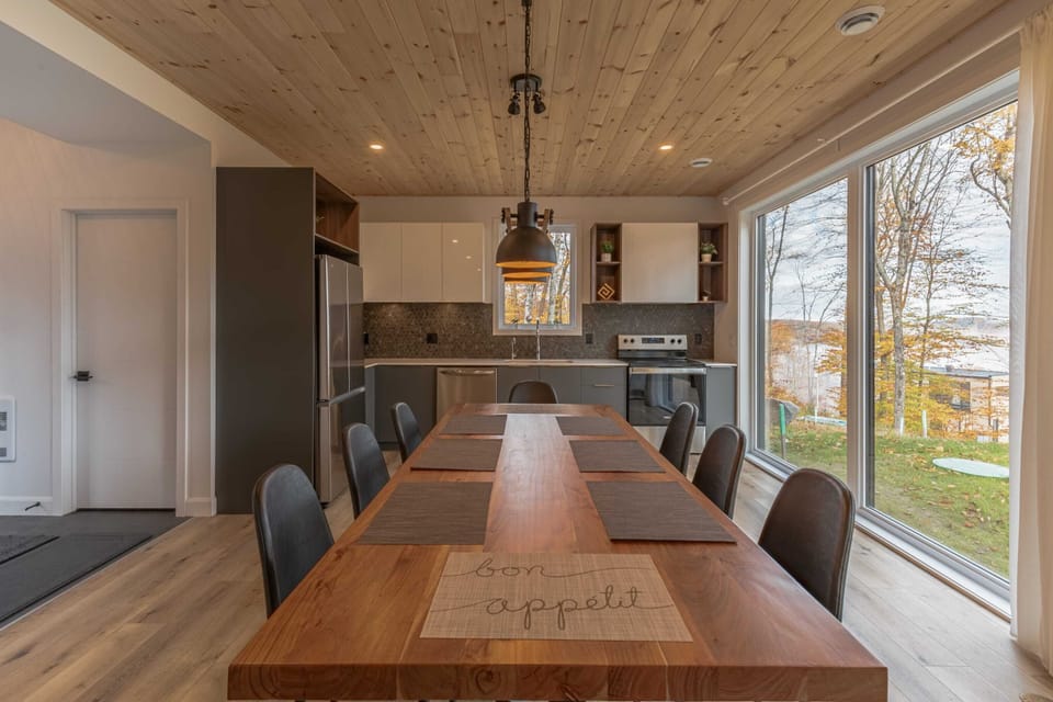 Dining table with pendant lighting beside large forest-facing windows