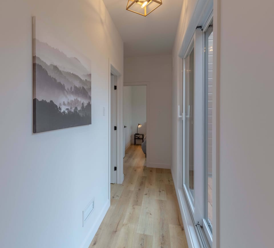 Bright hallway with wood flooring and large windows leading to a bedroom.