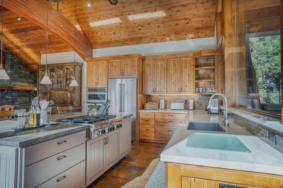 Kitchen with high end, stainless steel appliances, large stone island, farmhouse style sink, plenty of cabinets and large window that looks onto the top deck