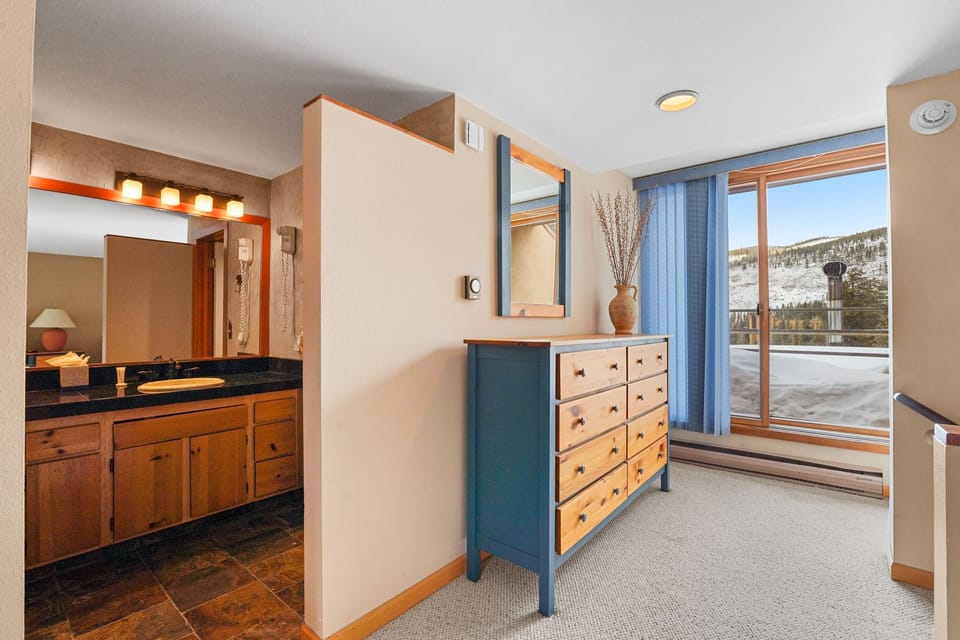 Your spacious bedroom features a cozy dresser and stunning mountain views through large windows, with a private ensuite bathroom nearby.