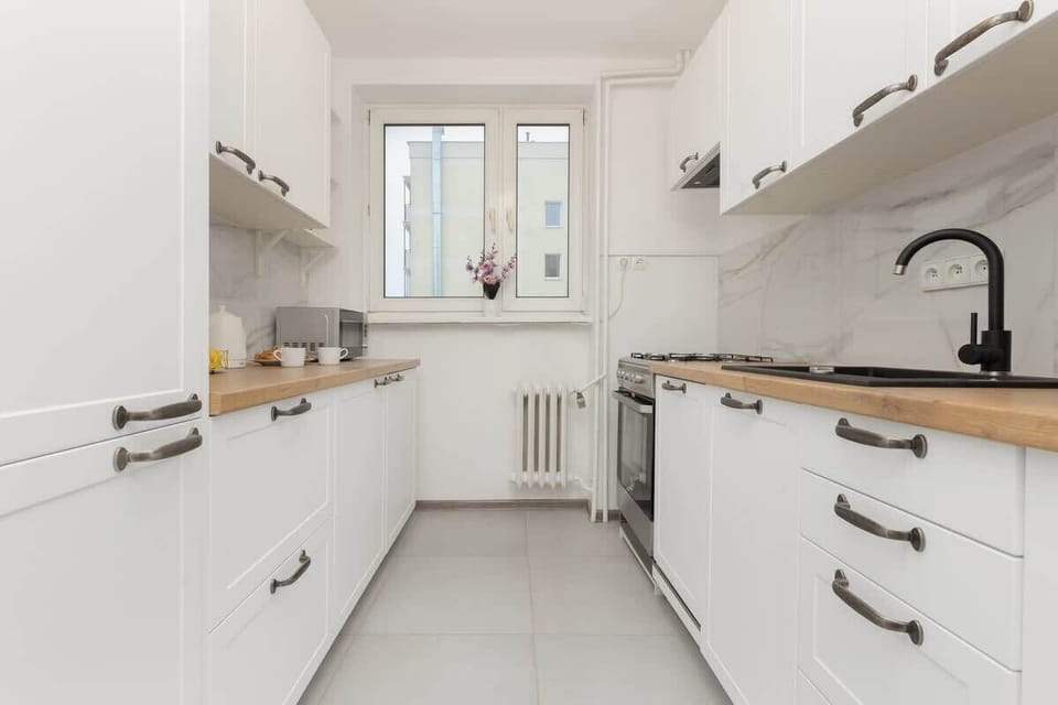A sleek, all-white kitchen with modern appliances, ample storage, and a large window providing daylight.