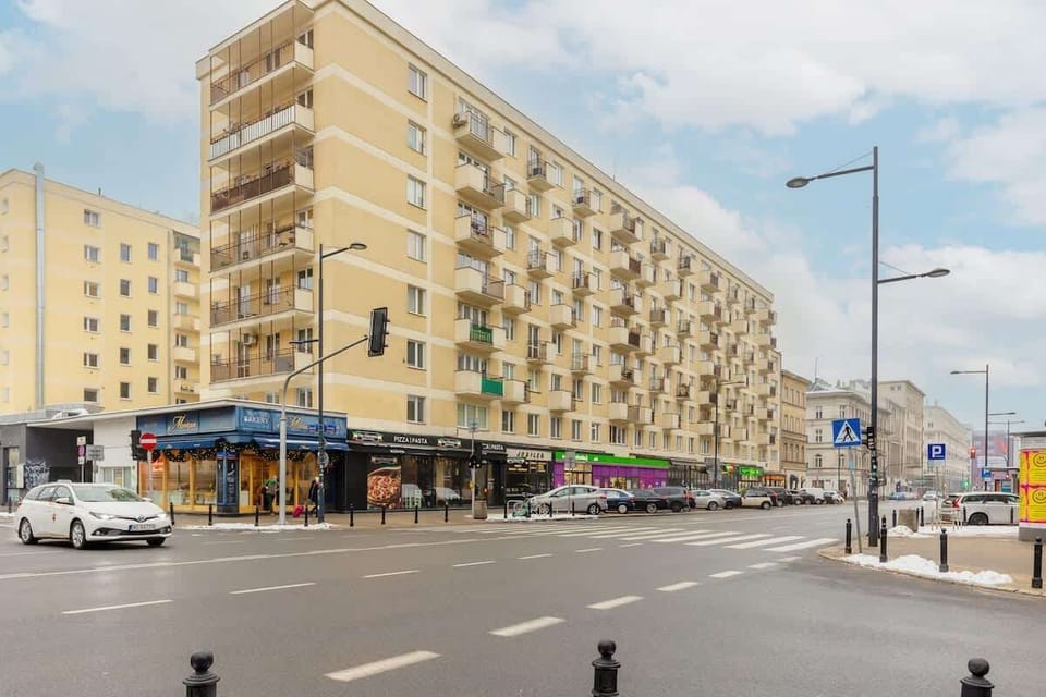 A street view of a modern residential building with shops on the ground floor and a lively city atmosphere.