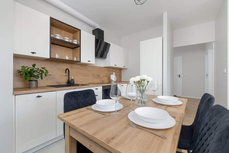 A modern kitchen with white cabinets, a wooden countertop, and a dining table with chairs.