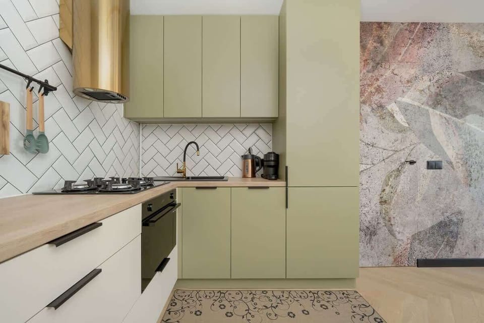 A contemporary kitchen with light green cabinetry, marble backsplash, and built-in appliances, offering ample cooking space.
