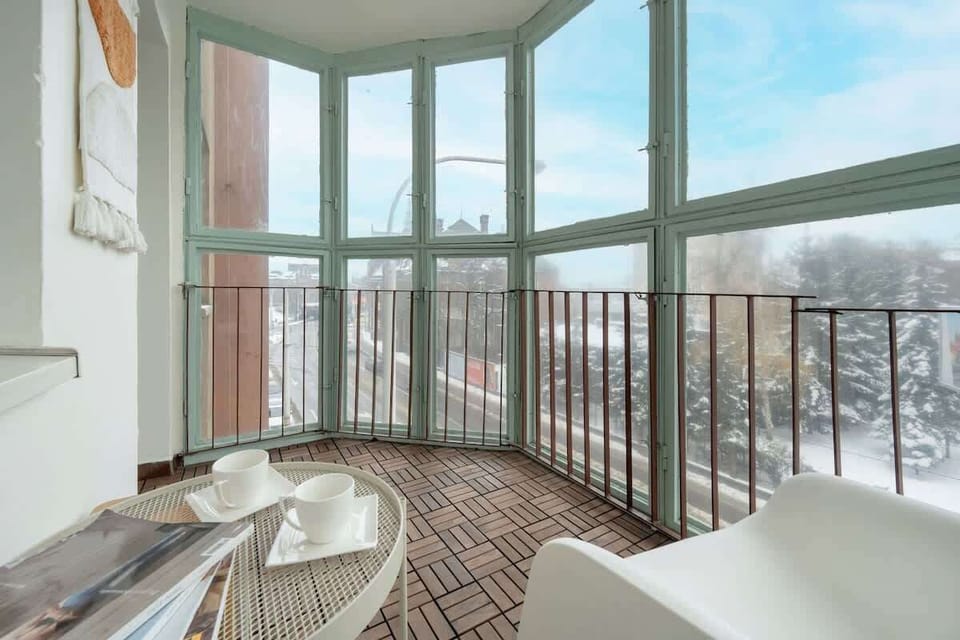A spacious enclosed balcony with large windows, a round table, and chairs.