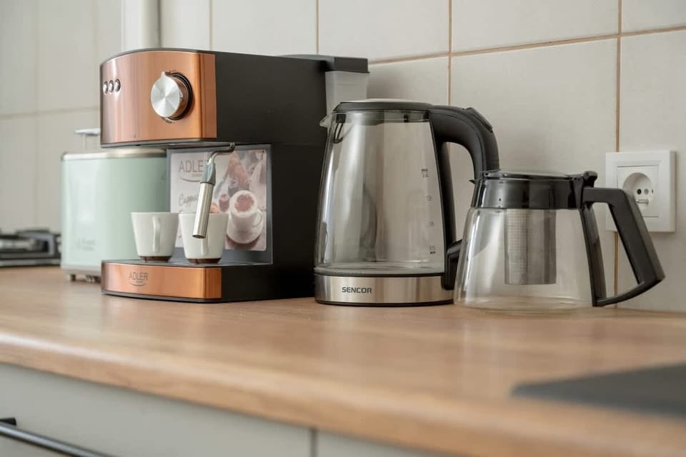 A wooden kitchen countertop with a kettle, coffee maker, and small appliances.