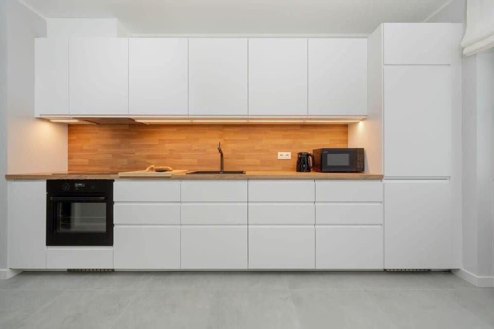 A fully equipped kitchen with white cabinetry and an orange backsplash, offering a sleek and modern design.
