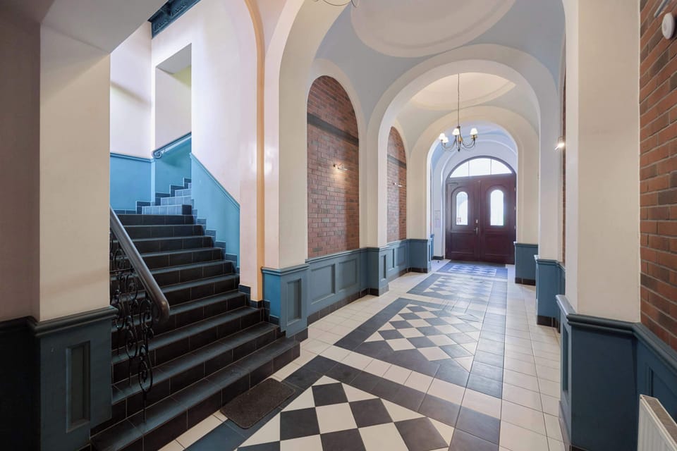 The elegant entrance hall with high arches, original geometric flooring, and classic stairs introduces the atmosphere of a historic townhouse, giving guests a unique first impression.