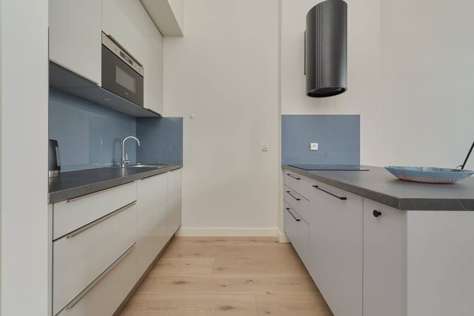 A fully equipped modern kitchen with sleek white cabinets, a blue backsplash, and essential appliances for a comfortable cooking experience.
