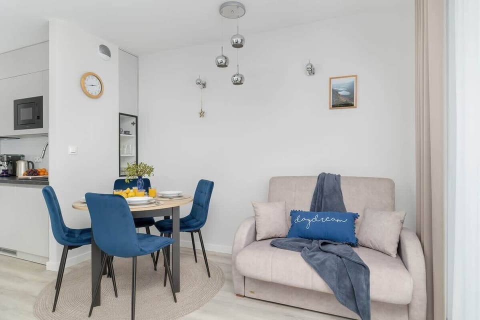 A cozy living room with a comfortable beige sofa, blue dining chairs, and a round dining table set for two, creating an inviting space for relaxation.

