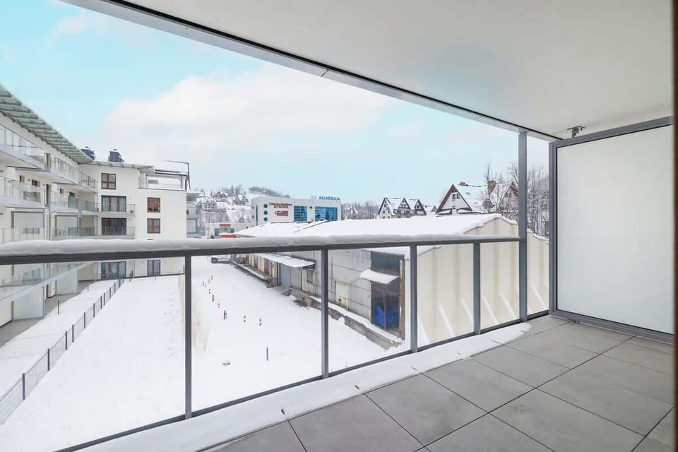 A wide balcony with a glass railing, offering a panoramic view of the residential area under a snowy sky.

