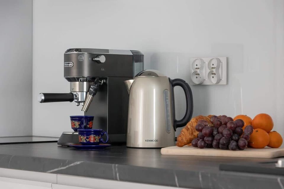 A coffee station featuring a coffee maker, electric kettle, and a bowl of fresh fruit, conveniently arranged on the kitchen countertop.

