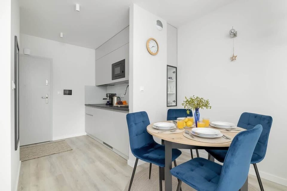 A bright kitchen and dining area with white walls, modern appliances, and a round dining table with blue chairs, maintaining a clean and airy feel.

