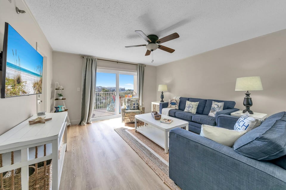 Welcome to Islander Beach Resort 311 - Sandy Dunes! Relax in your bright, coastal living room with comfy blue sofas and refreshing ceiling fan breezes.