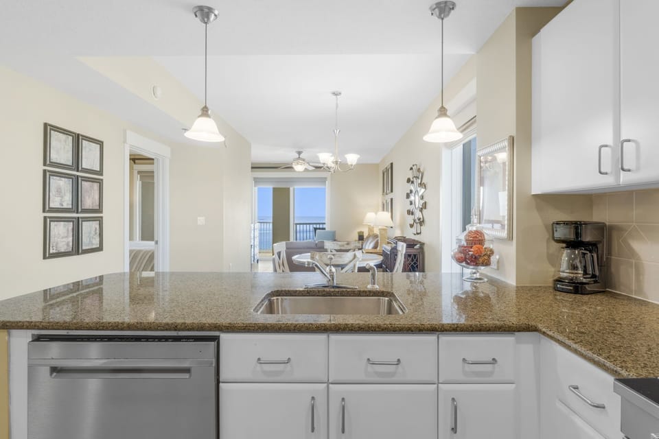 Modern kitchen with granite countertops overlooking a bright living and dining area.