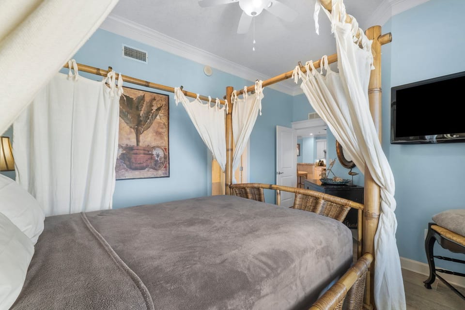 Relax in this cozy bedroom featuring a four-poster bed with light curtains and soft blue walls.