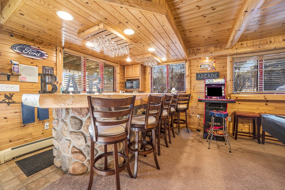 Arcade room bar—fully stocked with glasses, fridge, and bar seating