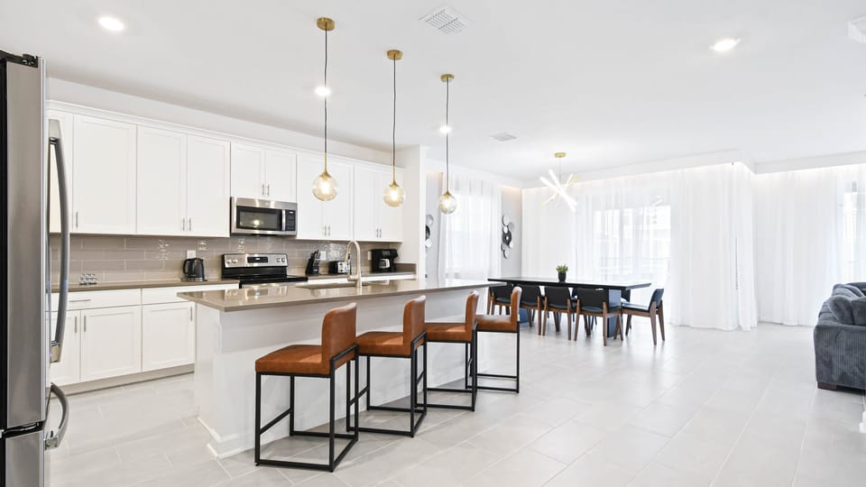 Bright open kitchen and dining space with island seating, modern lighting, and style.