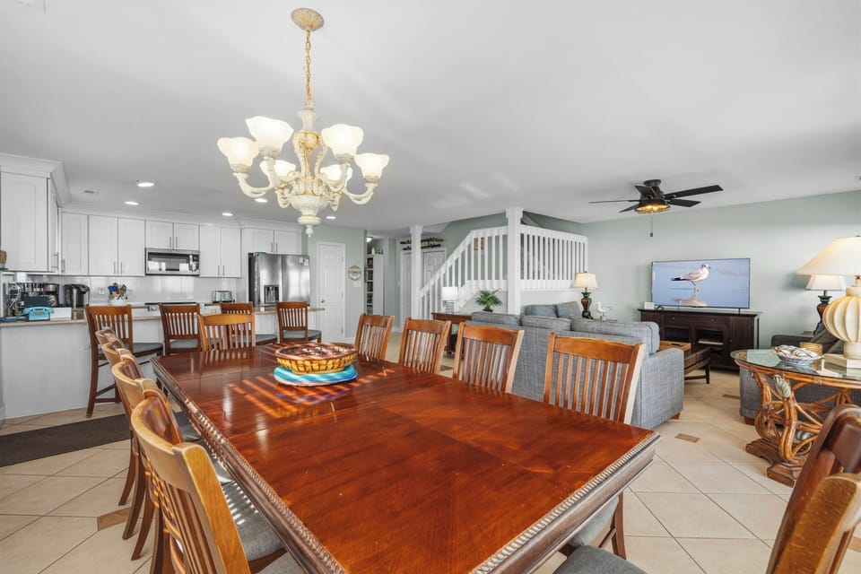 Gather around this grand dining table for memorable meals with your group, featuring elegant chandelier lighting and open flow to the kitchen.